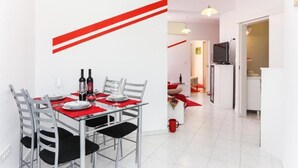 Un comedor moderno con una decoración en rojo y blanco, una mesa de comedor dispuesta con platos, vasos y botellas de vino, y una cocina visible al fondo.