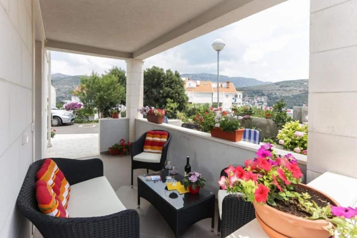 A balcony with wicker furniture, a table with a bottle, and potted plants.