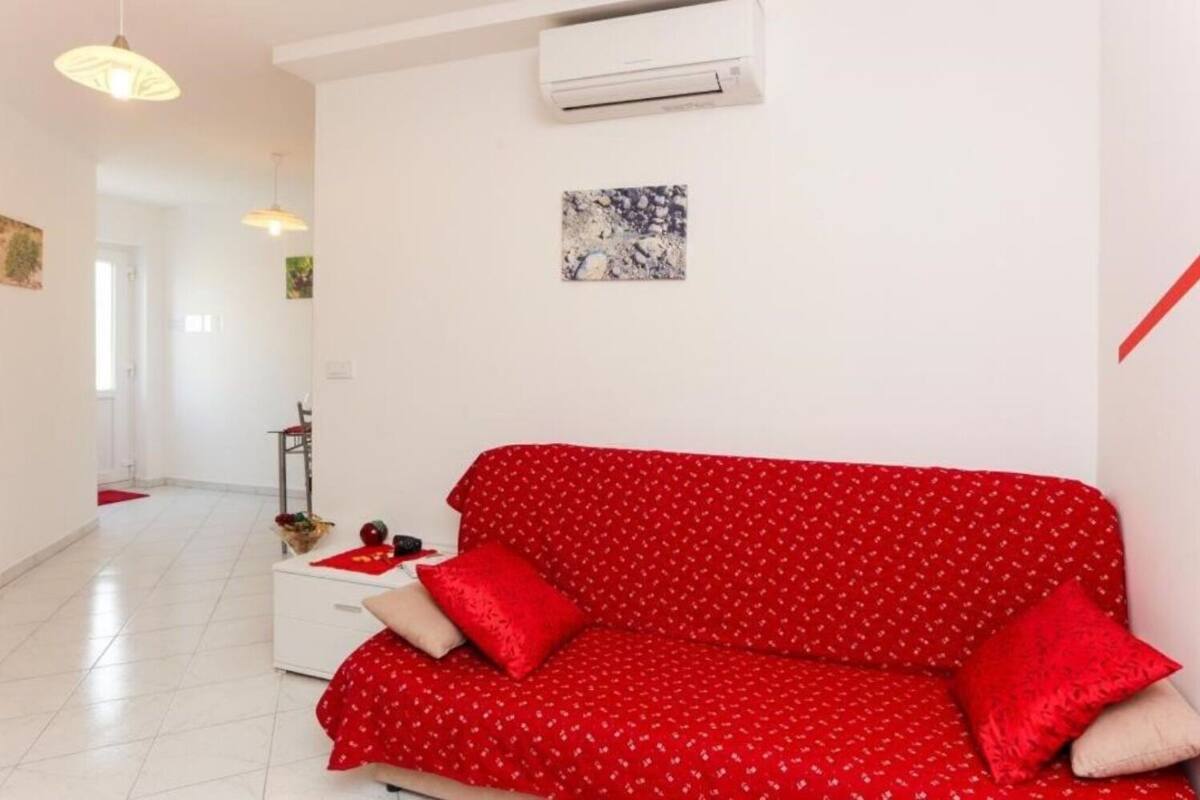 A living room with a red sofa, a white side table, and a small painting on the wall.