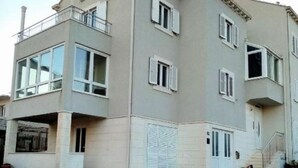 Un edificio residencial de varios pisos con un balcón en el segundo nivel, una puerta de garaje y una barrera de cuerda roja en primer plano.