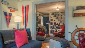Een woonkamer met een blauwe bank, een rode fauteuil, een houten schuttersrad en een vlag aan de muur.