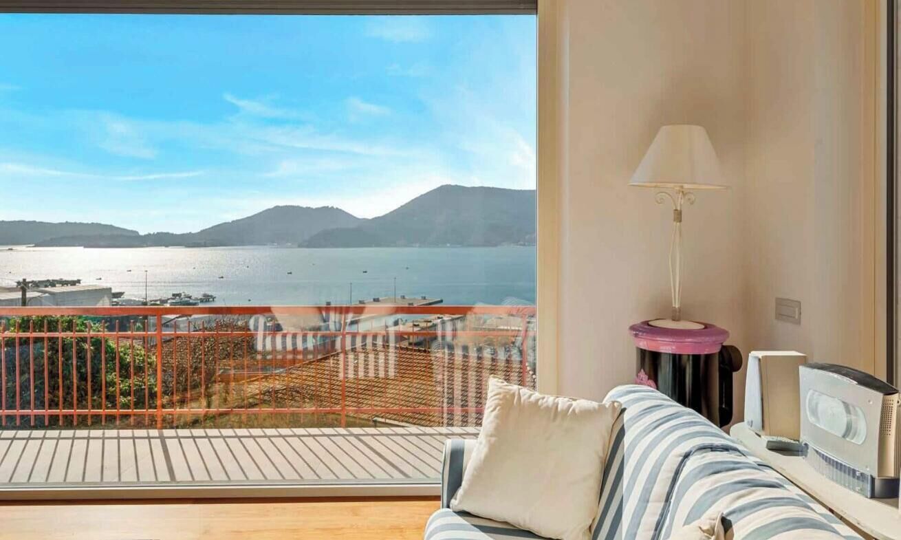 A balcony with a view of a body of water and mountains, a sofa with a lamp, and a speaker.