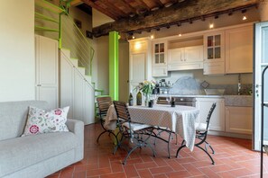 A cozy living room with a sofa, a dining table with chairs, a staircase with green railings, and a kitchen area with cabinets and a countertop. - Executive apartment in Borgo di Matraia (Matraia)