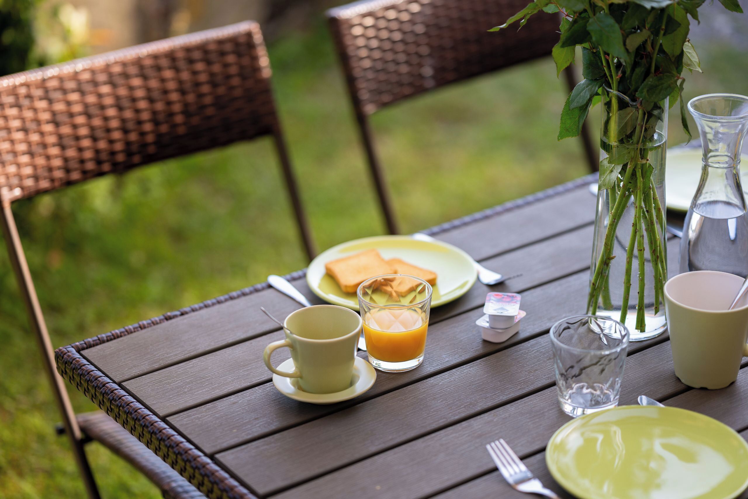 A table set with a plate of food, a glass of orange juice, a cup, a glass of water, and a vase with green plants.