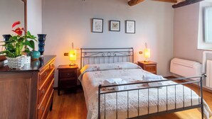 A bedroom with a wooden ceiling, a bed with a floral bedspread, bedside lamps, a dresser, and a mirror. - Executive apartment in Borgo di Matraia (Matraia)