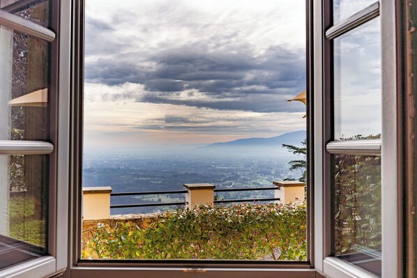Ein Fenster mit Blick auf eine Stadtlandschaft und Berge unter einem bewölkten Himmel.
