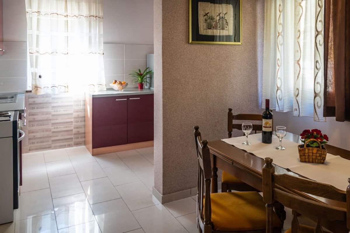 Un coin repas avec une table dressée pour deux personnes, une bouteille de vin et un panier de fleurs.