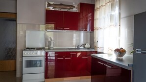 A kitchen with red cabinets, a white stove, and a window with curtains. - Apartments Dar (Lokve)