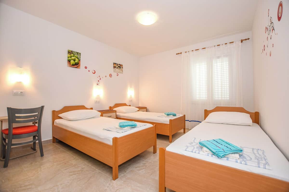 A hotel room with three wooden beds, a chair, and a small table.