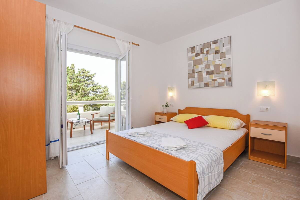 A bedroom with a wooden bed, a balcony with a table and chairs, and a view of greenery outside.