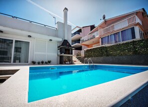 A modern pool area with a clear blue pool, a covered outdoor kitchen, and a staircase leading to a balcony. - House Nepi (Rogoznica)