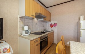 A compact kitchen with wooden cabinets, a built-in oven, a sink, and a refrigerator. - Apartments Dusan (Rab)