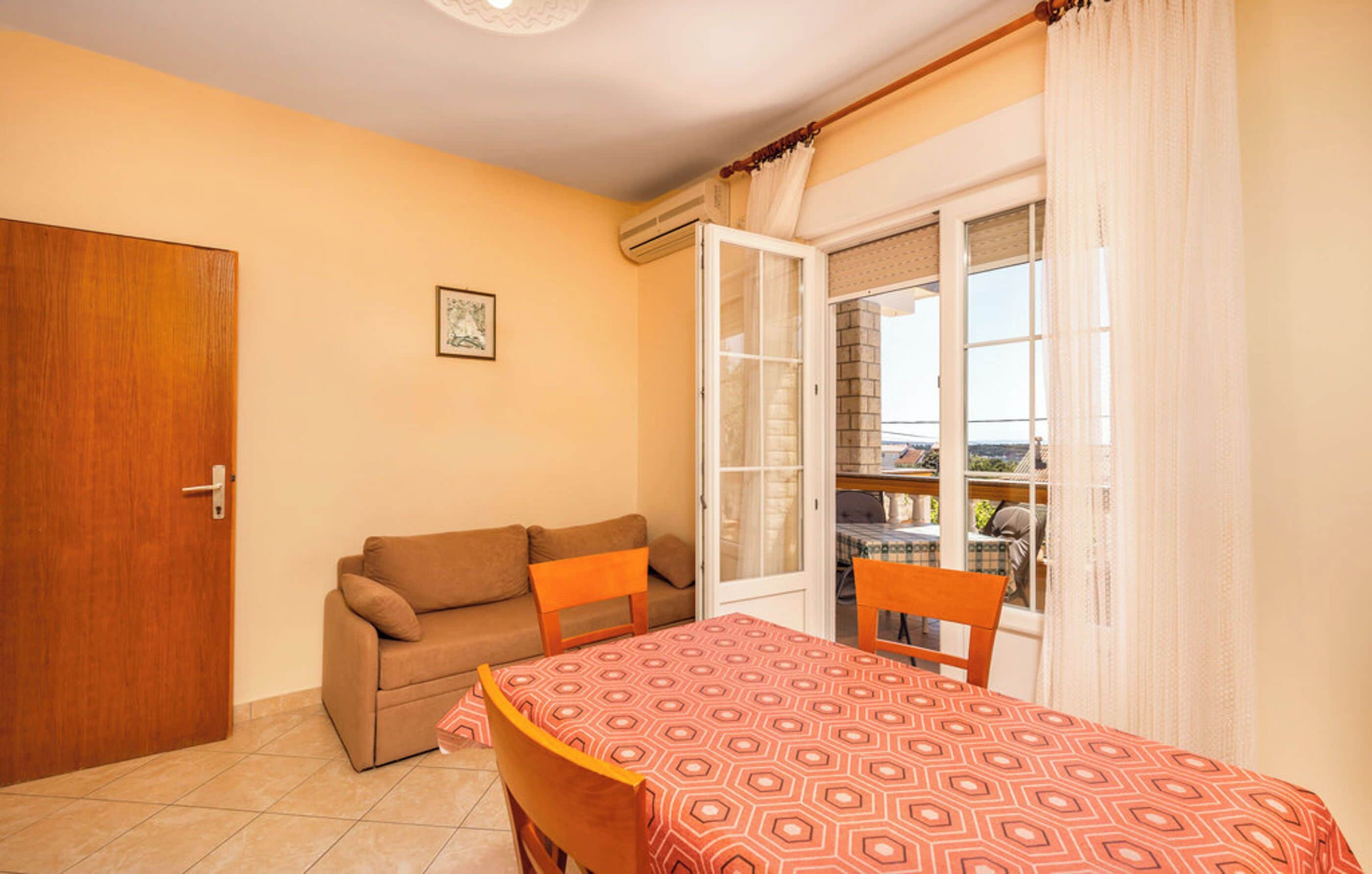 A room with a sofa, a dining table with a patterned tablecloth, a door, and a window with curtains.