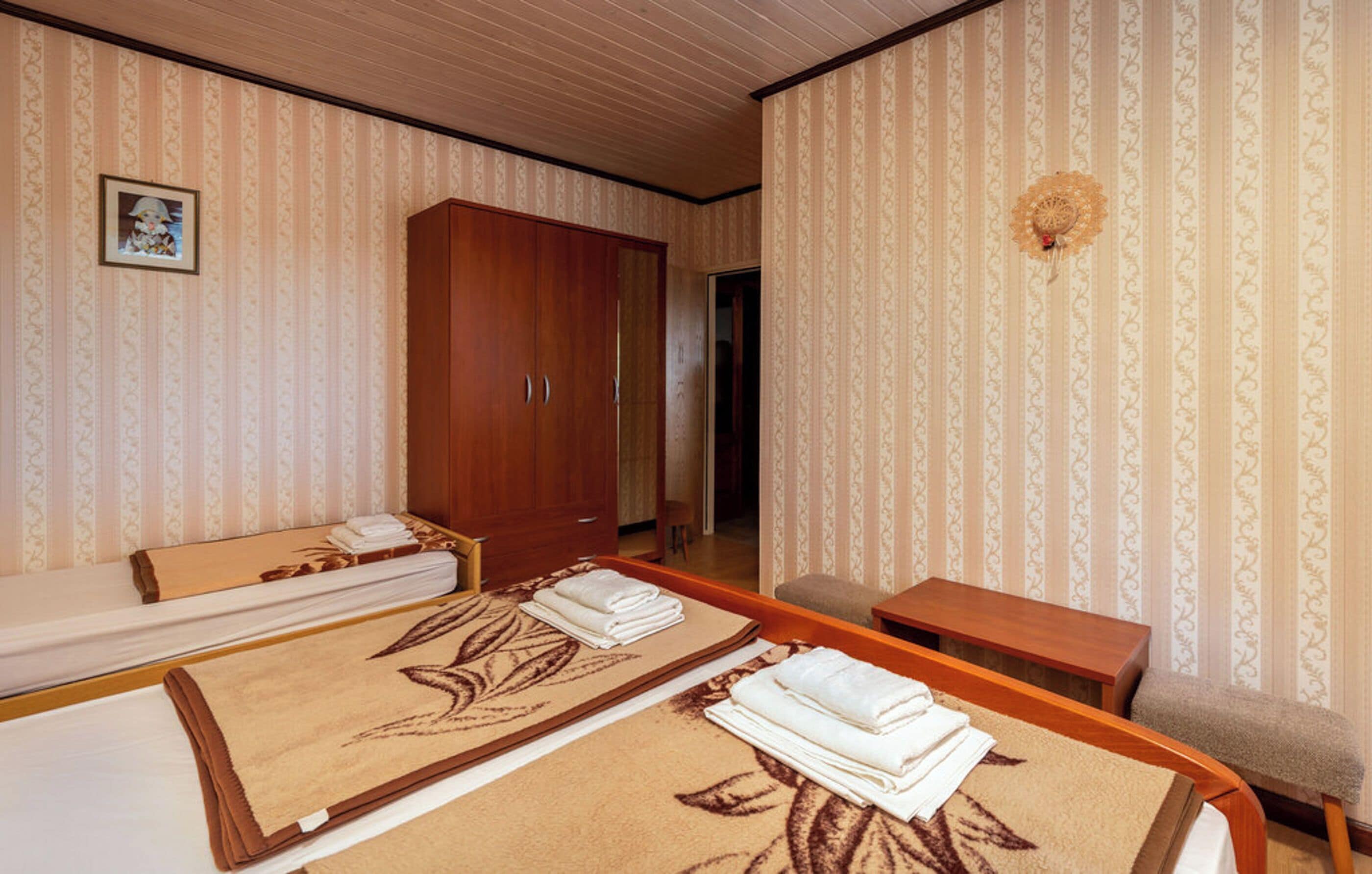 A hotel room with two beds, a wooden wardrobe, a small table, and a decorative wall piece.