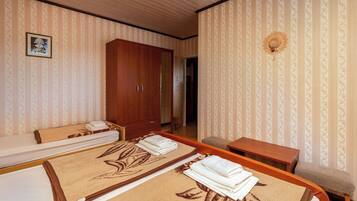 A hotel room with two beds, a wooden wardrobe, a small table, and a decorative wall piece.