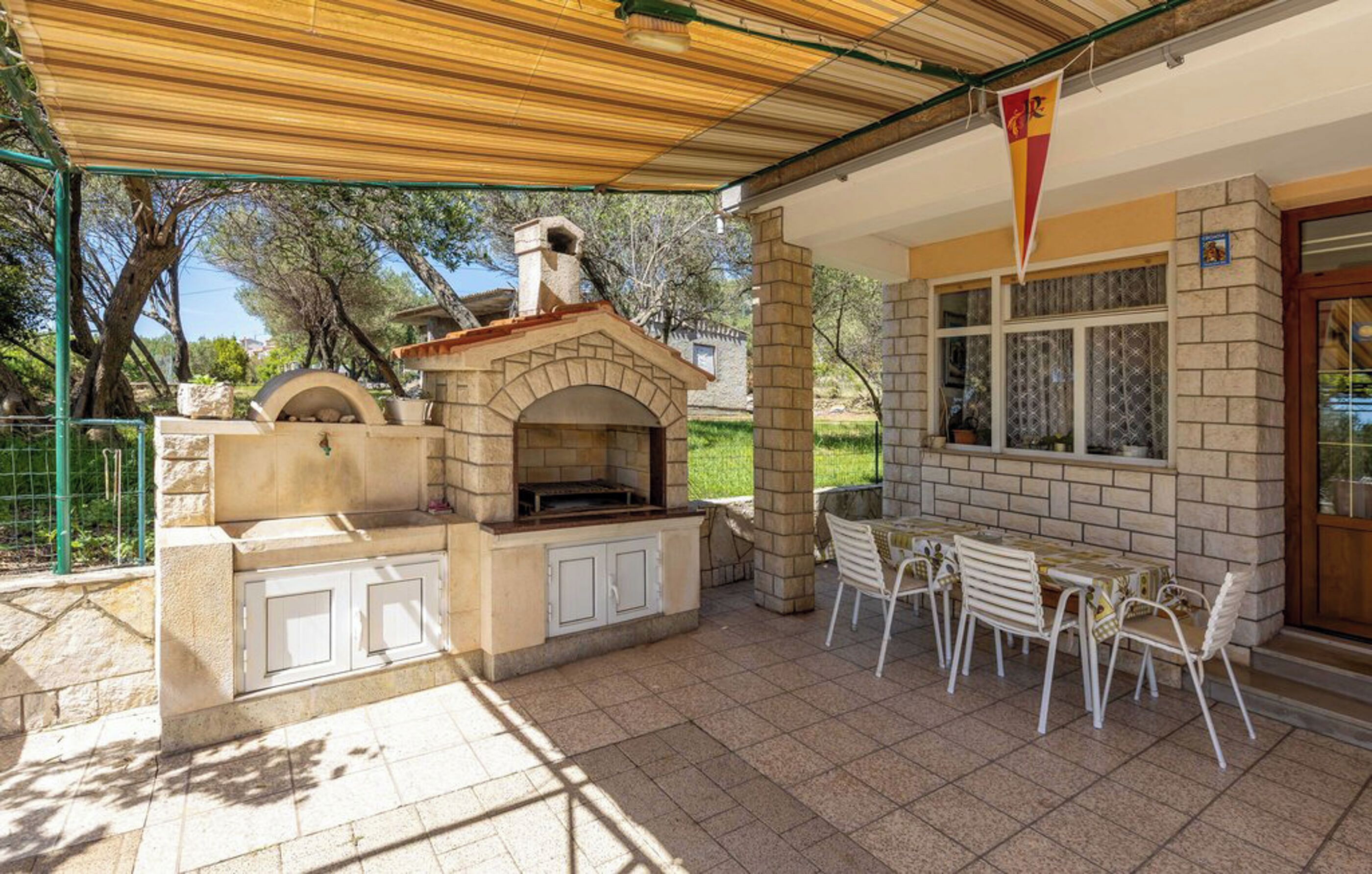 An outdoor patio with a brick oven, white chairs, and a table.