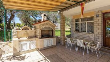 An outdoor patio with a brick oven, white chairs, and a table.