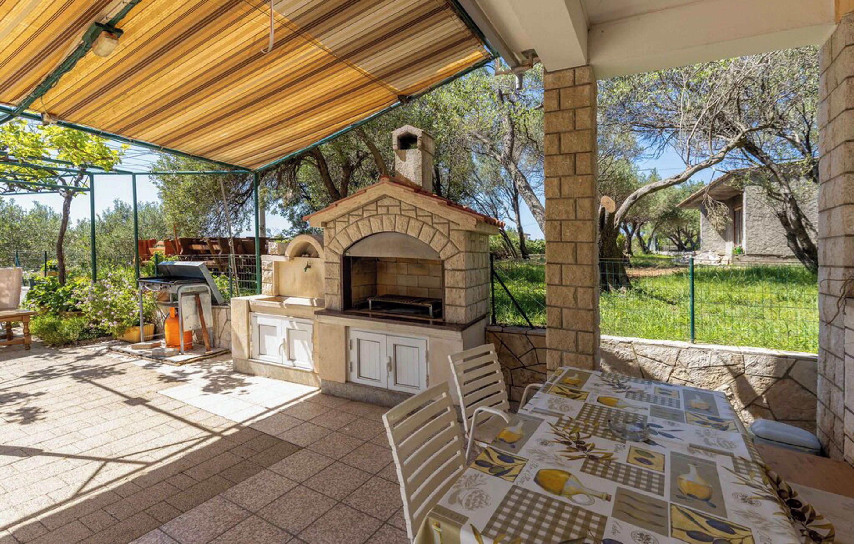 An outdoor patio with a stone barbecue and grill, a table with a placemat, and a pergola overhead.
