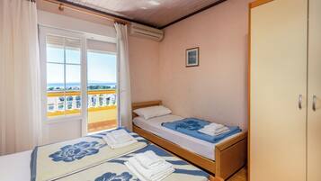 A room with two beds, a wardrobe, a window with curtains, and a balcony.