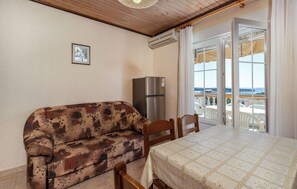 A room with a patterned sofa, a table with a lace tablecloth, a refrigerator, and a view through a glass door. - Apartments Dusan (Rab)