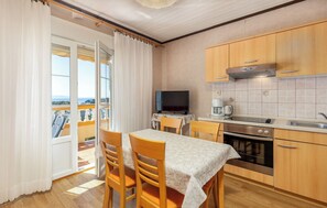 A room with a balcony, a dining table with chairs, a television, a kitchen with wooden cabinets, and a tiled backsplash. - Apartments Dusan (Rab)