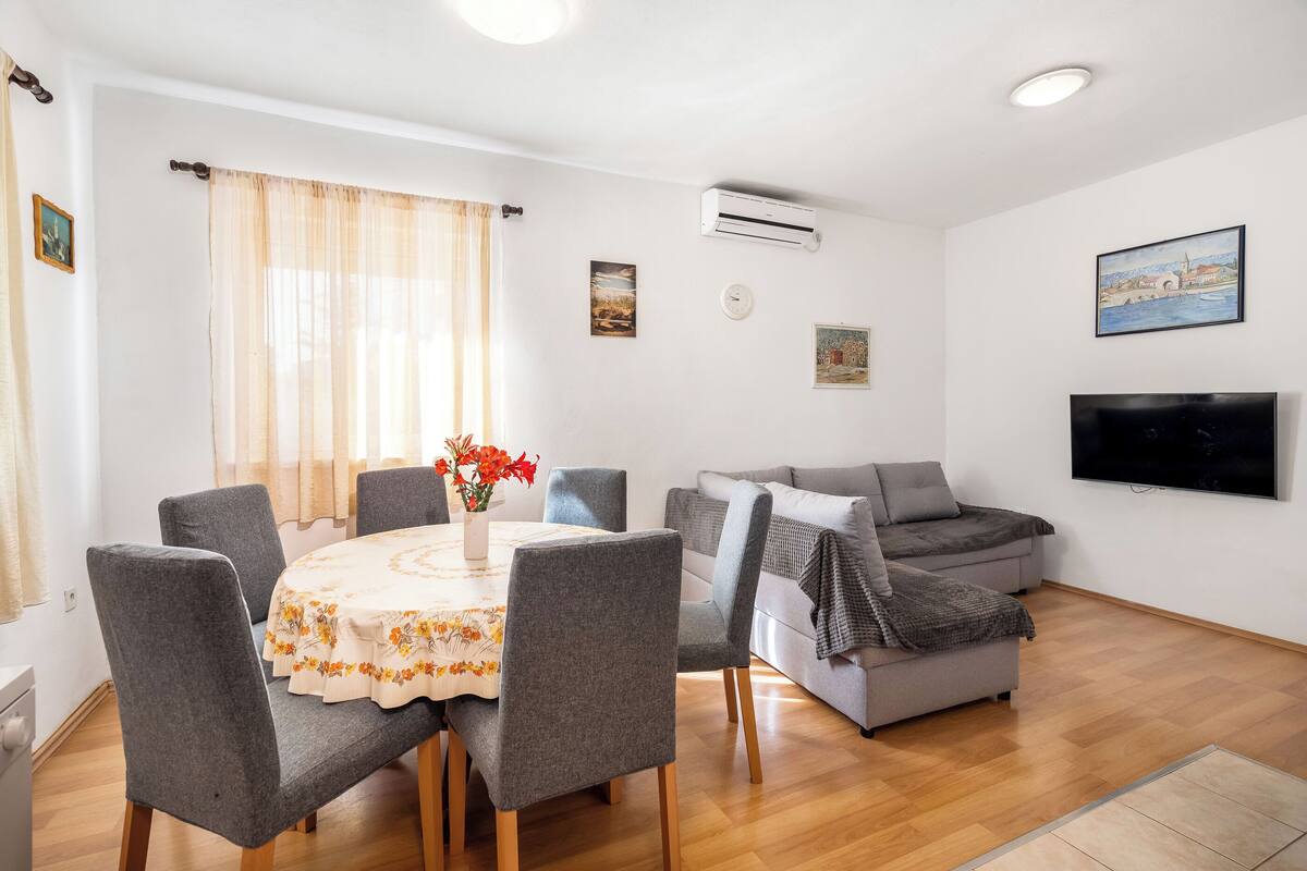 A modern living room with a dining table, grey chairs, a grey sofa, and a flat-screen TV mounted on the wall.