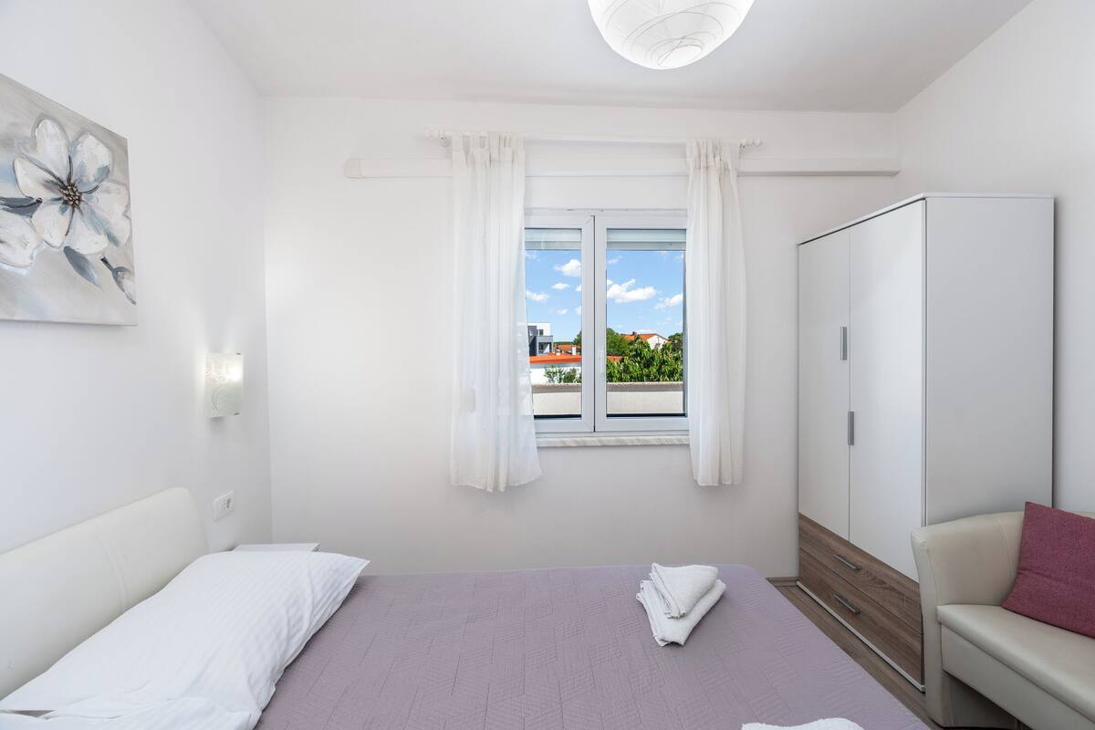 A bedroom with a bed, a wardrobe, a window with curtains, and a painting on the wall.
