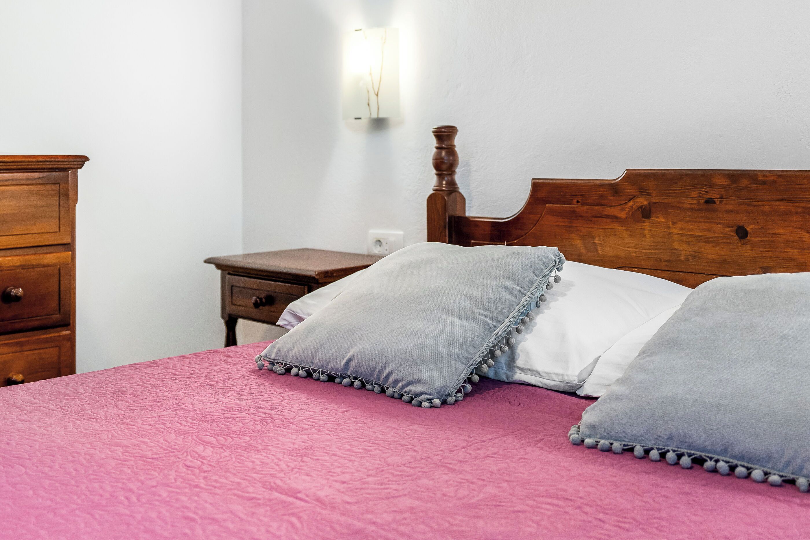 A bed with a wooden headboard, a pink bedspread, and two pillows with tassels.