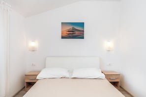 A minimalist hotel room with a bed, two bedside tables, and a wall-mounted picture of a mountain. - Apartment Baras (Nin)