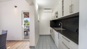 A modern kitchen with white cabinets, a black countertop, and a tiled floor. - Apartment Baras (Nin)