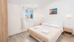 A bedroom with a bed, a nightstand, a window with curtains, and a wall-mounted picture. - Apartment Baras (Nin)