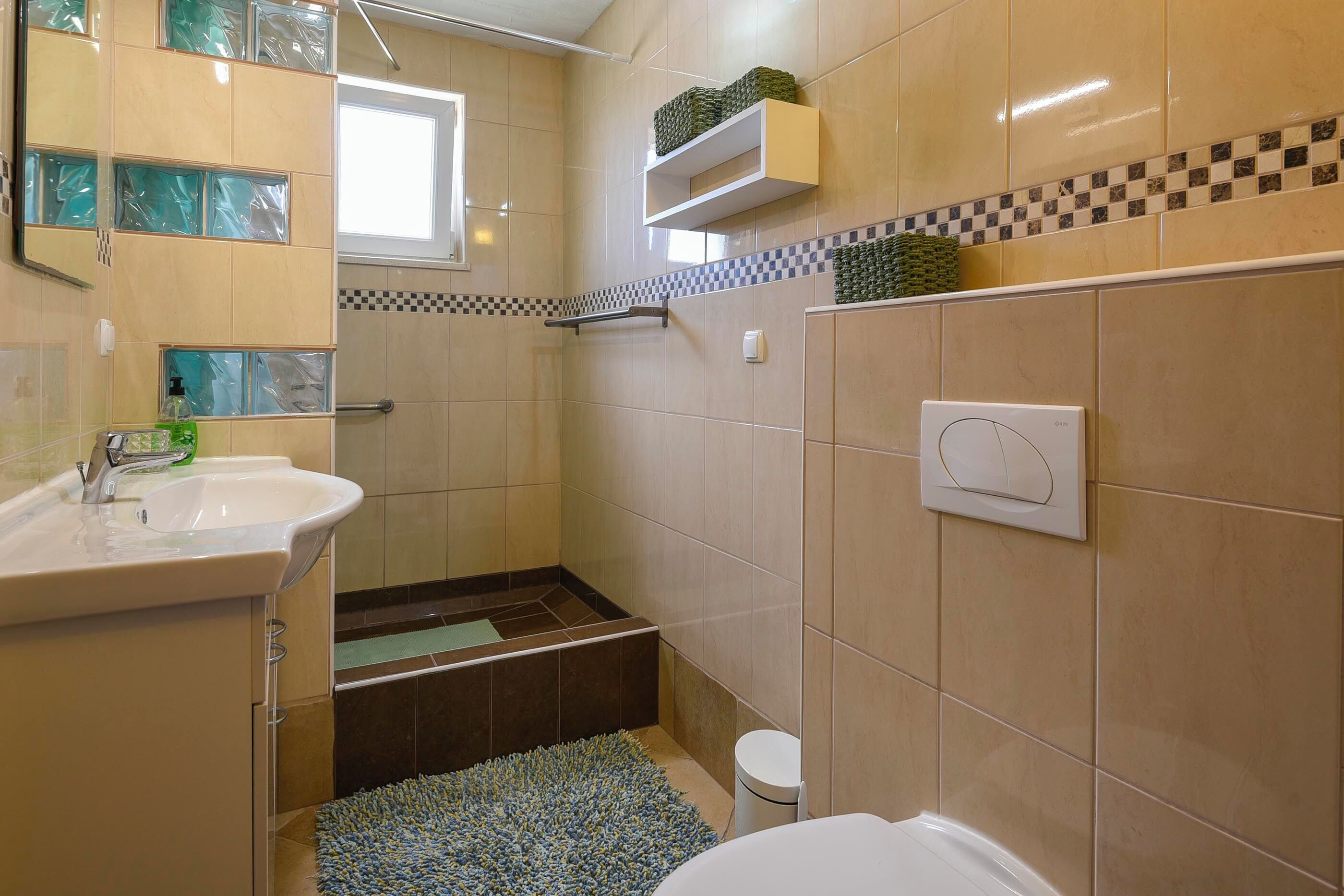A bathroom with a sink, toilet, shower, and a small window.