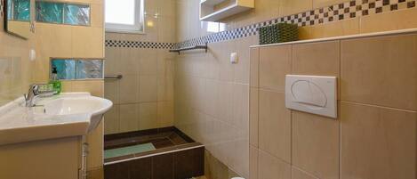 A bathroom with a sink, toilet, shower, and a small window.