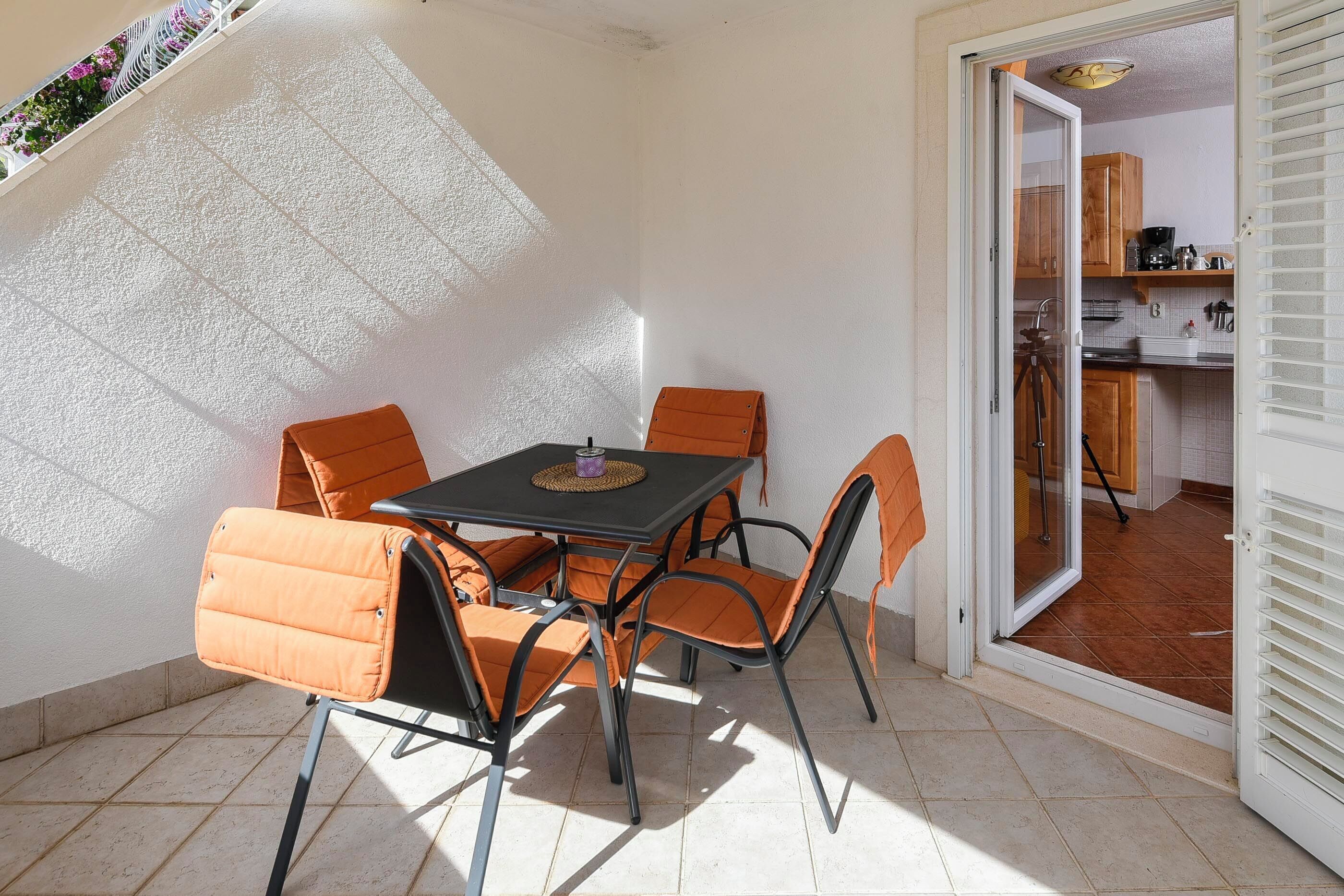 A patio with a table and chairs, a sliding door to a kitchen, and a tiled floor.