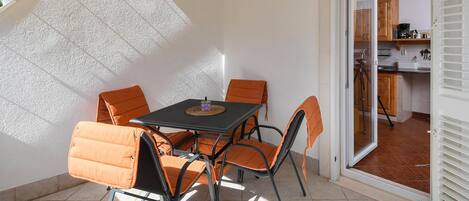 A patio with a table and chairs, a sliding door to a kitchen, and a tiled floor.