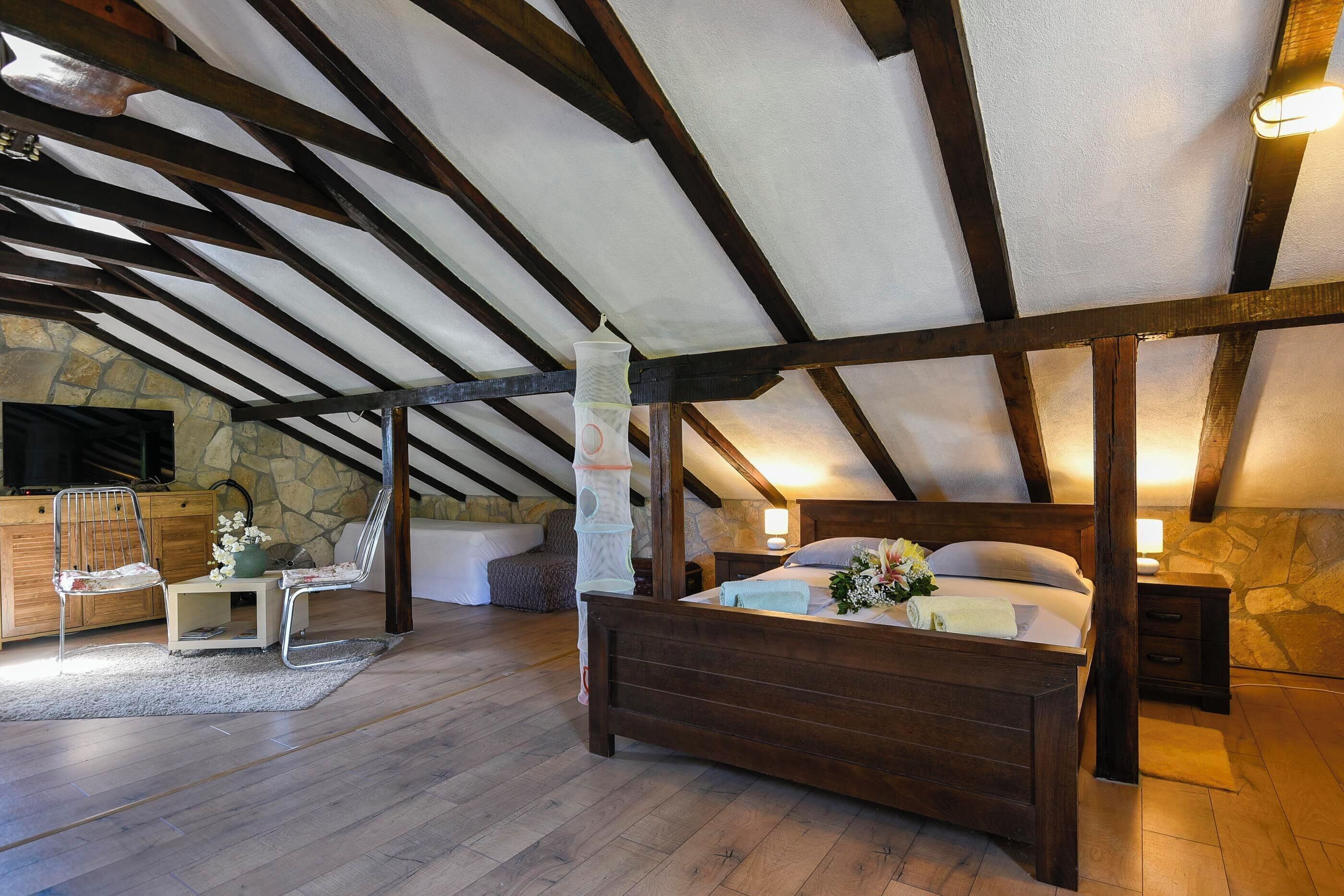 A bedroom with a wooden bed, stone walls, and a sloped ceiling with exposed beams.