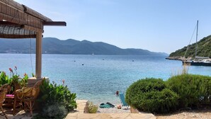 Une terrasse en bord de mer, meublée de mobilier en osier, avec une piscine et une vue sur la mer et les montagnes.