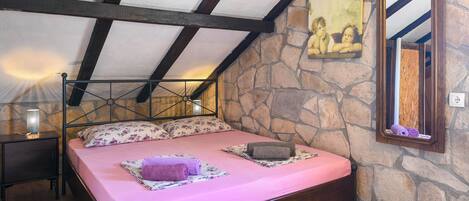 Ein Schlafzimmer mit Steinsturz, einem Bett mit rosa Bettwäsche, einem Holz-Kopfstück, einem Nachttisch, einer Lampe und einem Spiegel.