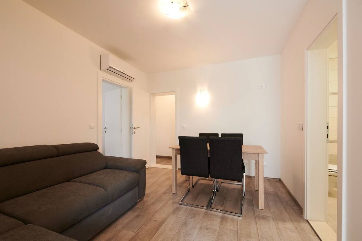 A living room with a sofa, a dining table with chairs, and a door with an air conditioning unit.