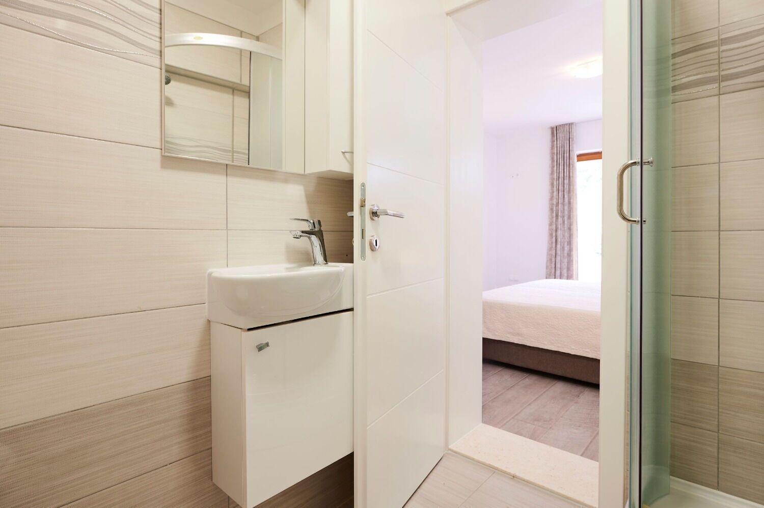 A modern bathroom with a white sink, mirror, and a glass shower enclosure.