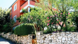 A two-story building with a stone wall and a well-maintained garden with flowering trees.