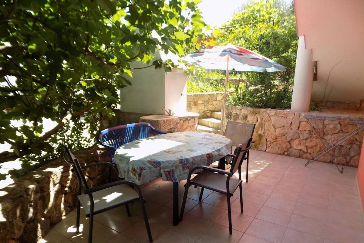 Eine Terrasse mit einem runden Tisch, vier Stühlen, einer Steinmauer und einem Sonnenschirm.