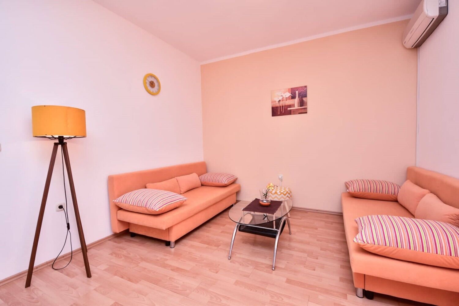 Un salon avec deux canapés orange, une petite table, un lampadaire et une horloge murale.