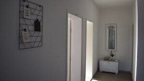 En hall med ett geometriskt väggkonstverk, en vit dörr och ett litet vitt skåp med en spegel.