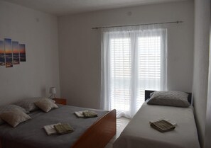 A room with two beds, a nightstand, a lamp, and a window with blinds.