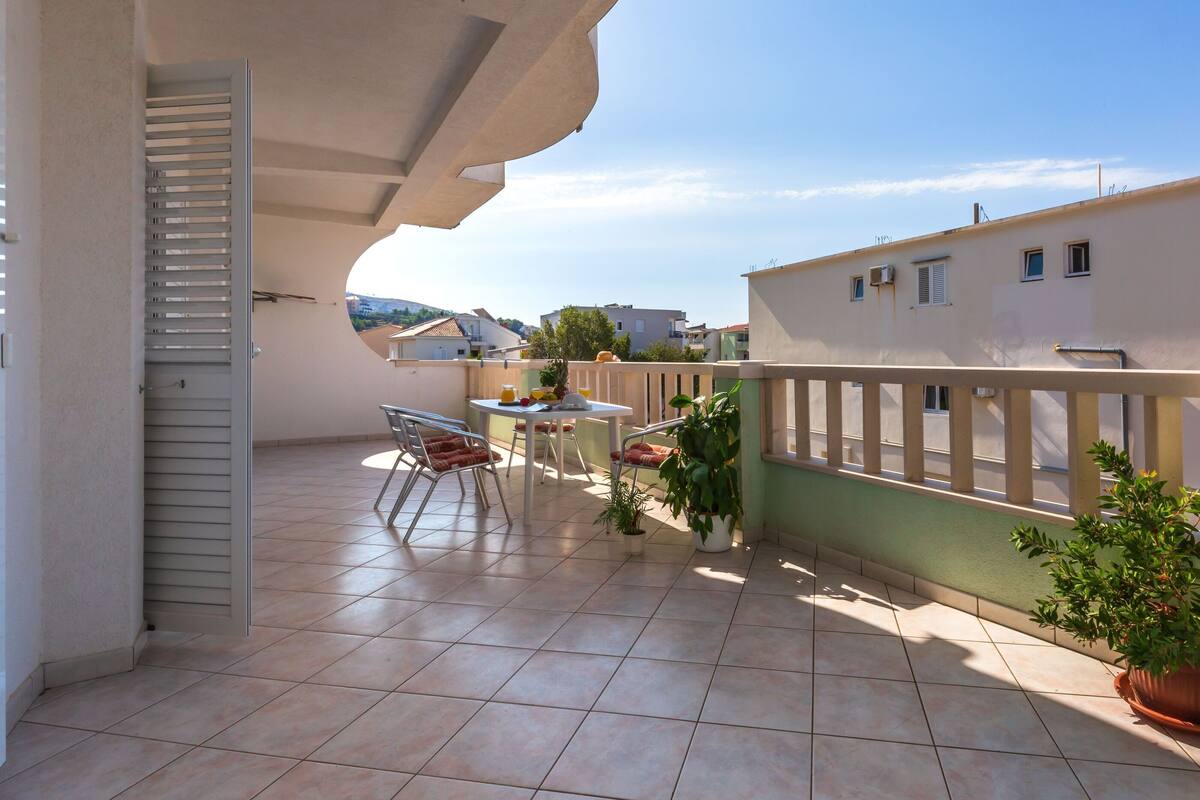 A balcony with a tiled floor, a table with chairs, and potted plants.