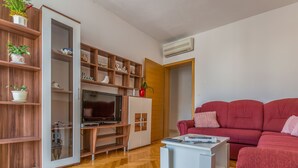 A living room with a red sofa, a white coffee table, a TV, wooden shelves, and a cabinet. - Apartments and Rooms Happiness (Tucepi)