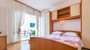 A bedroom with a wooden bed, a small desk, and a balcony with a table and chairs. - Apartments and Rooms Happiness (Tucepi)