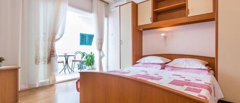 Une chambre avec un lit en bois, un petit bureau et un balcon équipé d’une table et de chaises.