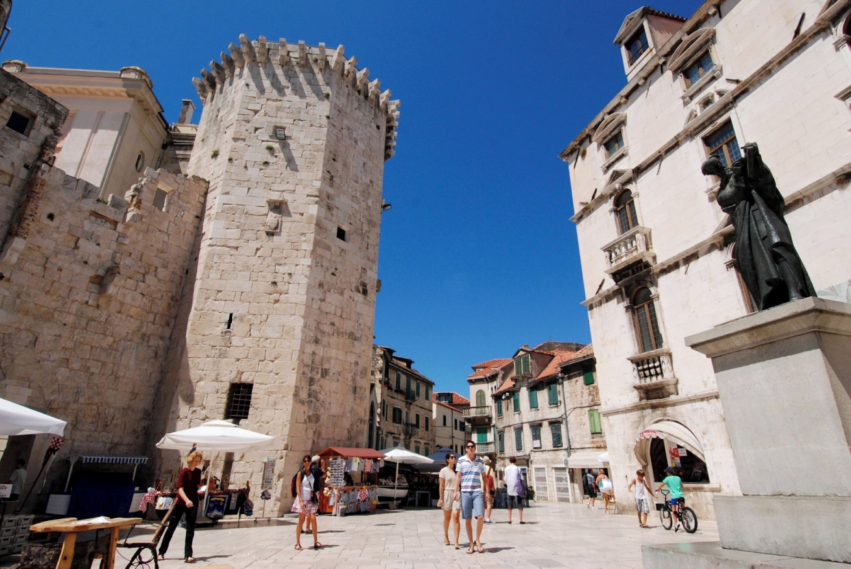 A historic stone tower, a paved square, and traditional buildings with balconies.